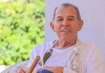 Foto Chico Lacerda, com alguns instrumentos de percussão na mão e sorrinso;